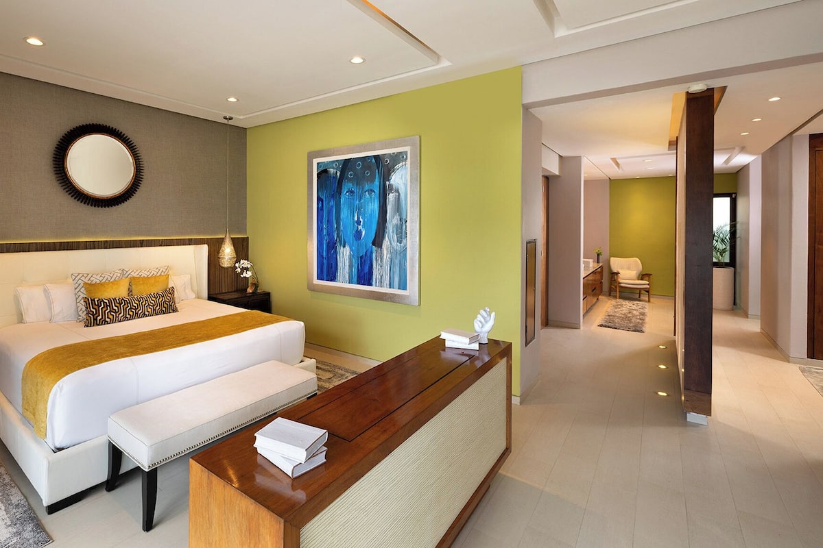 A modern bedroom with a large bed, bedside tables, a desk, and a painting on the wall.