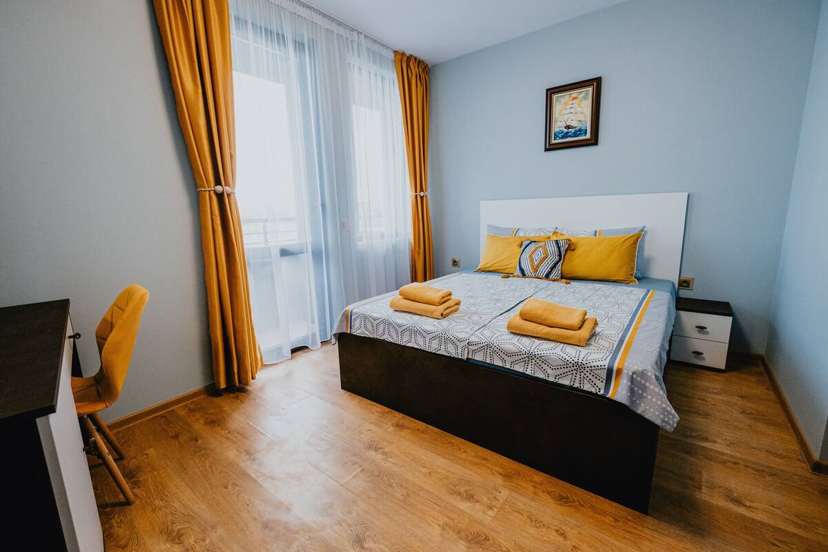 A bedroom with a bed, a chair, a nightstand, and a window with curtains.