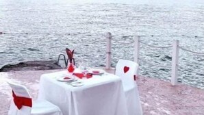 A table set for two with white tablecloths and red heart decorations, overlooking a body of water.