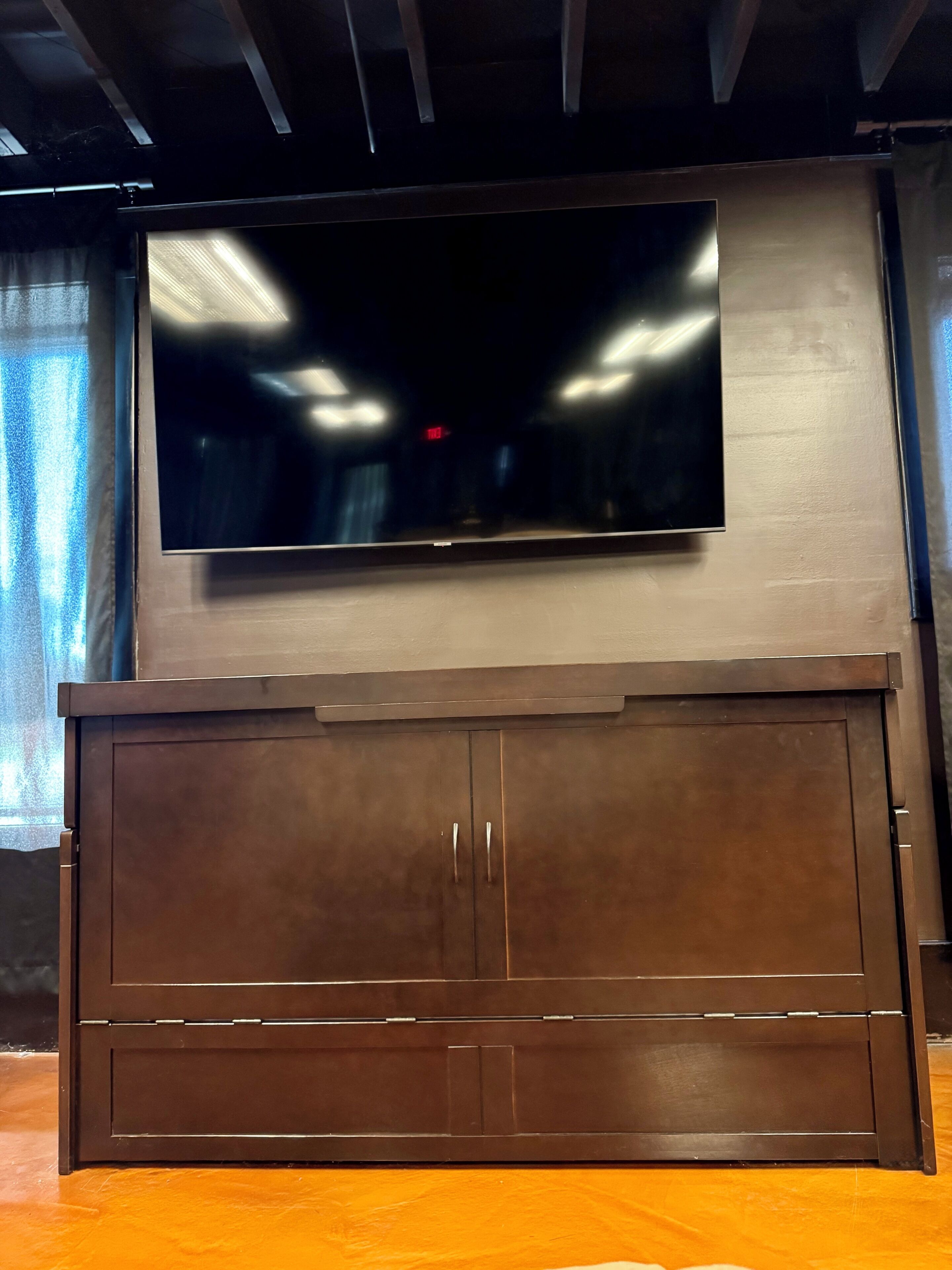 A flat-screen TV mounted on a wooden cabinet with two doors.