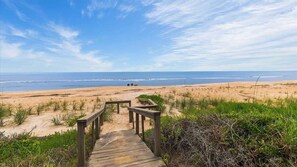 A wooden boardwalk leading to a beach with a clear sky.