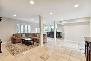 A spacious living room with a beige tiled floor, a brown sectional sofa, and a coffee table.