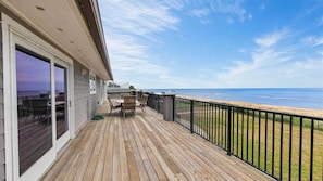Una terraza de madera con vistas al océano, mobiliario exterior y una barandilla.