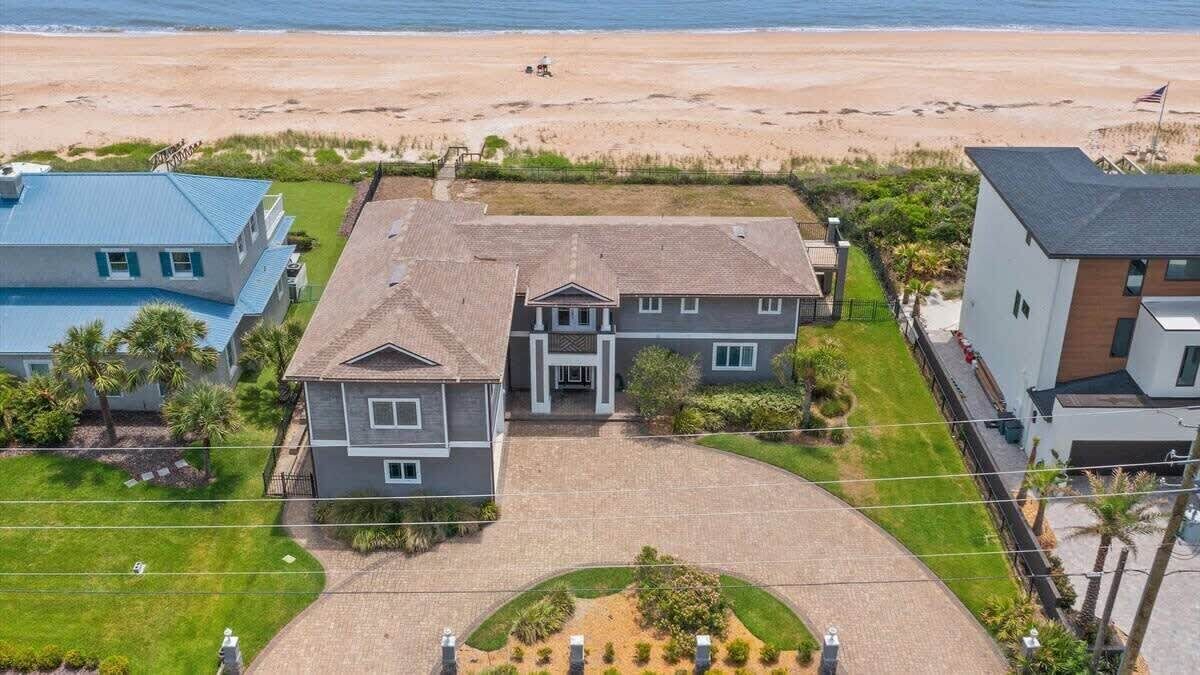 A large house with a driveway, a lawn, and a view of the beach.