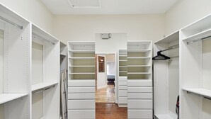Ein begehbarer Kleiderschrank mit offenen Regalen, ein Staubsauger und ein Holzboden.