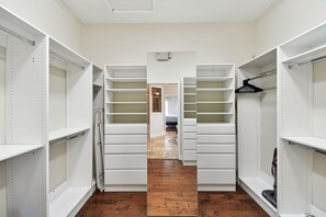 Um closet espaçoso com prateleiras abertas, um aspirador de pó e piso de madeira.