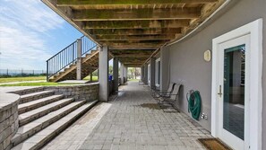 A covered outdoor area with a stone staircase leading to a deck, a green hose, and a door with a window.