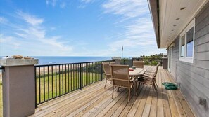 Una terraza de madera con mesa y sillas, con vista a una playa y al océano.