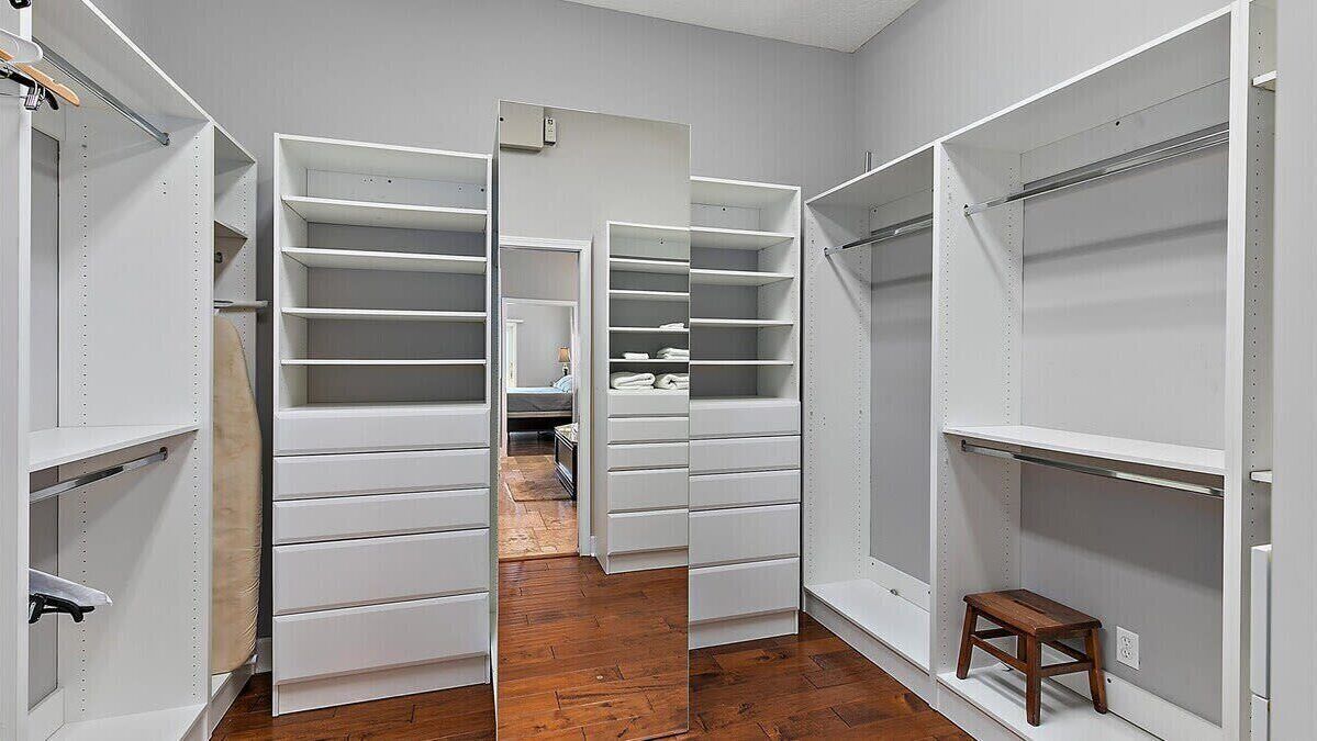 A walk-in closet with open doors, wooden flooring, and a small stool.