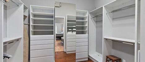 A walk-in closet with open doors, wooden flooring, and a small stool.
