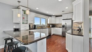 A modern kitchen with white cabinetry, a large island with stools, and a stainless steel refrigerator.