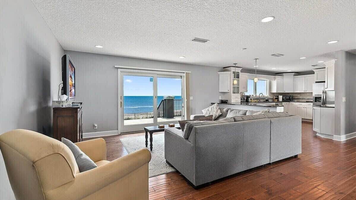A spacious living area with a grey sofa, a beige armchair, and a view of the ocean through large sliding doors.