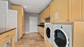 A laundry room with two front-loading washing machines, wooden cabinets, a white door, and a tiled floor.