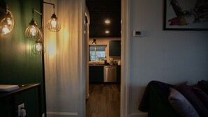 A narrow hallway with a kitchen at the end, featuring a window, stainless steel appliances, and a green wall. - An Alluring Escape (Cincinnati)