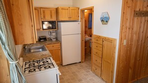 A compact kitchen with wooden cabinets, a microwave, a refrigerator, a gas stove, and a coffee maker.