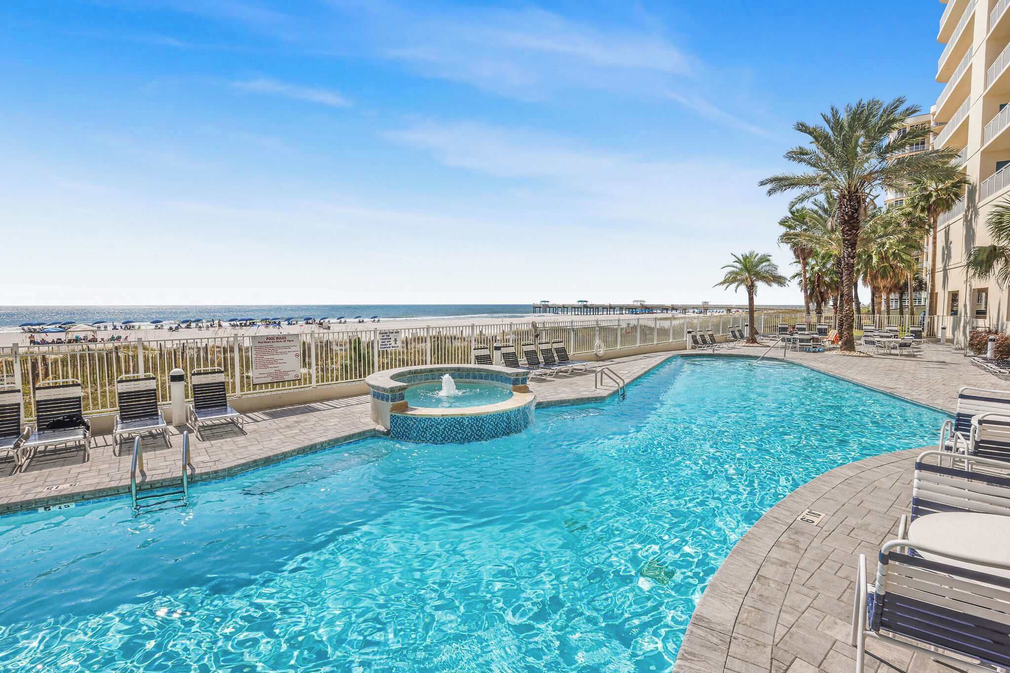 A pool with a hot tub, lounge chairs, and a view of the beach.