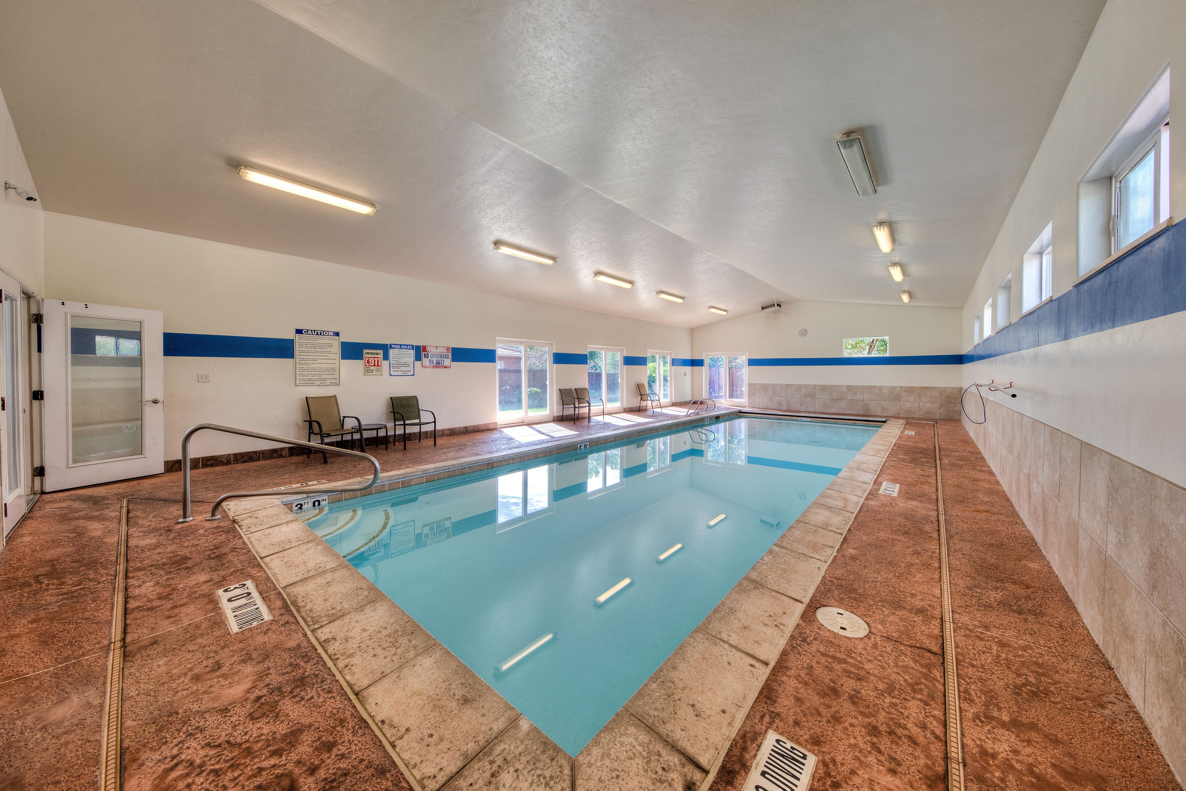 A large indoor swimming pool with clear blue water, surrounded by walls with blue and white stripes, and a ceiling with fluorescent lighting.