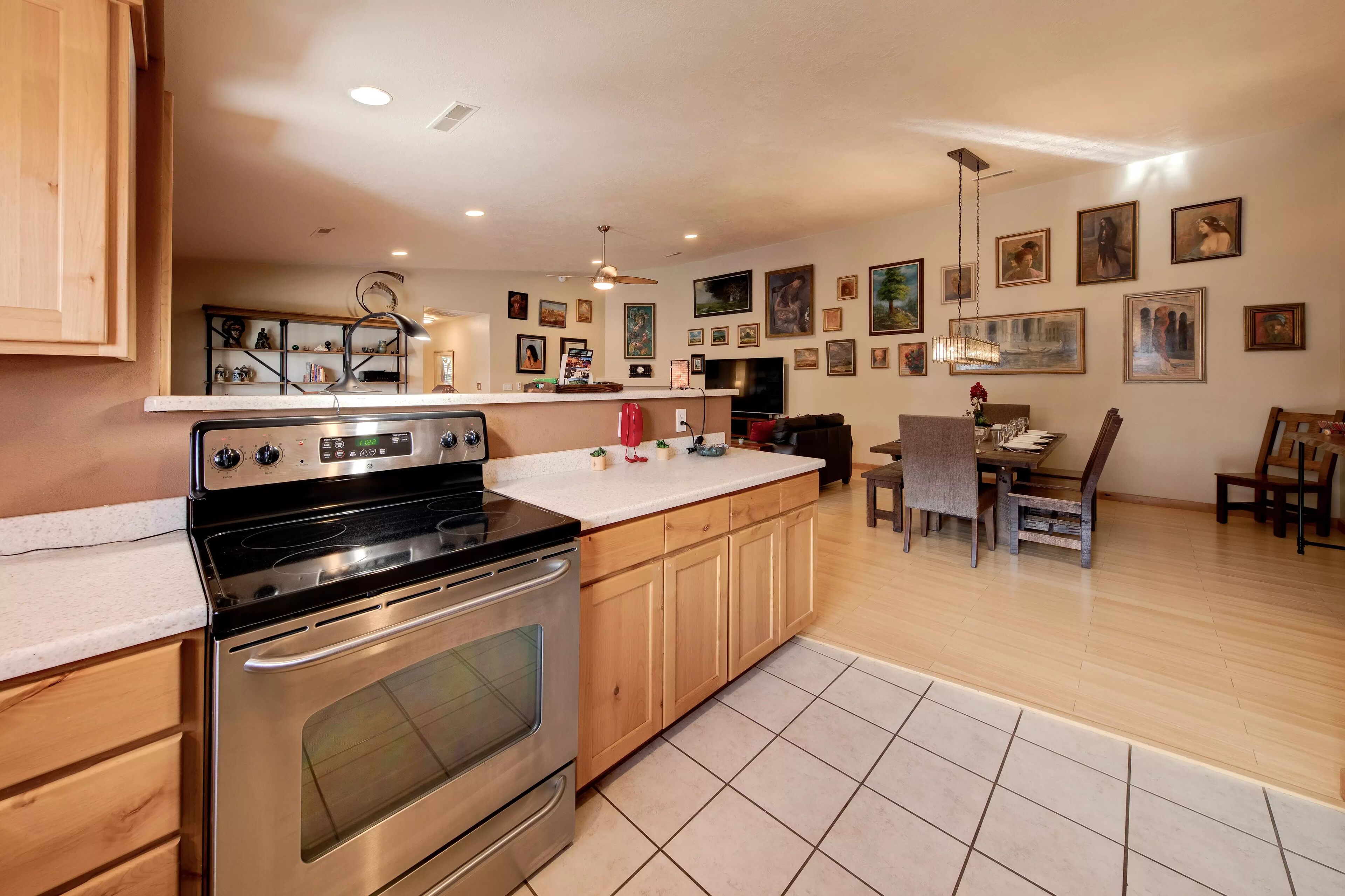 A modern kitchen with wooden cabinets, a stainless steel stove, and a dining area with a table and chairs.
