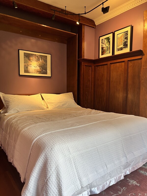 A bedroom with a large bed, wooden headboard, and two framed pictures on the wall. - Beautiful heritage home suite on main floor in Nelson's best location. Upscale. (Nelson)