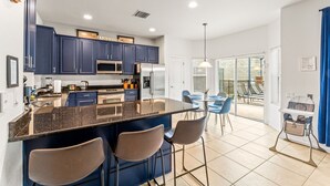 Una cucina moderna con mobili scuri blu, un'isola centrale con sgabelli da bar e una zona pranzo con sedie blu.