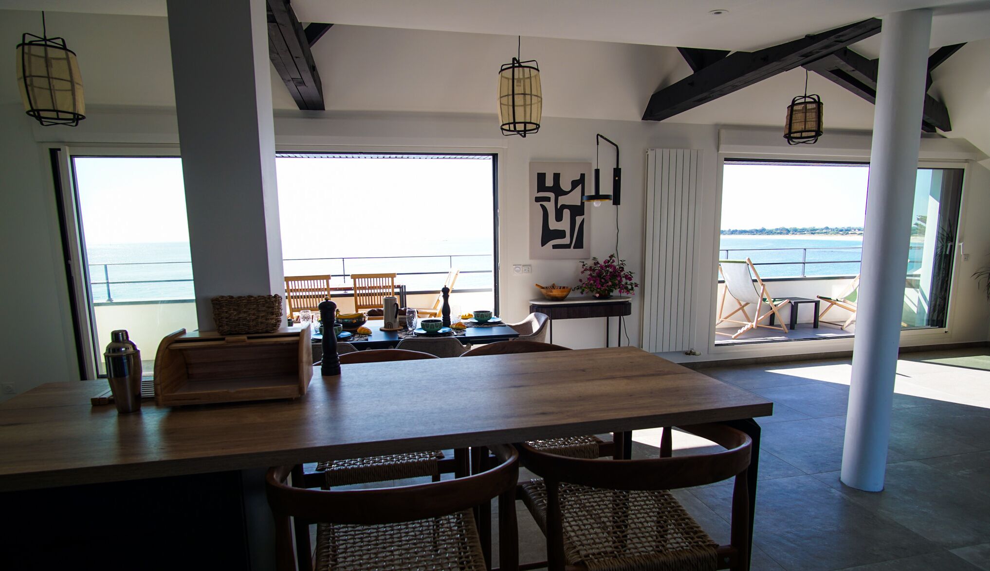 Un amplio comedor con una gran mesa de madera, sillas de mimbre y vista al mar a través de grandes ventanales.