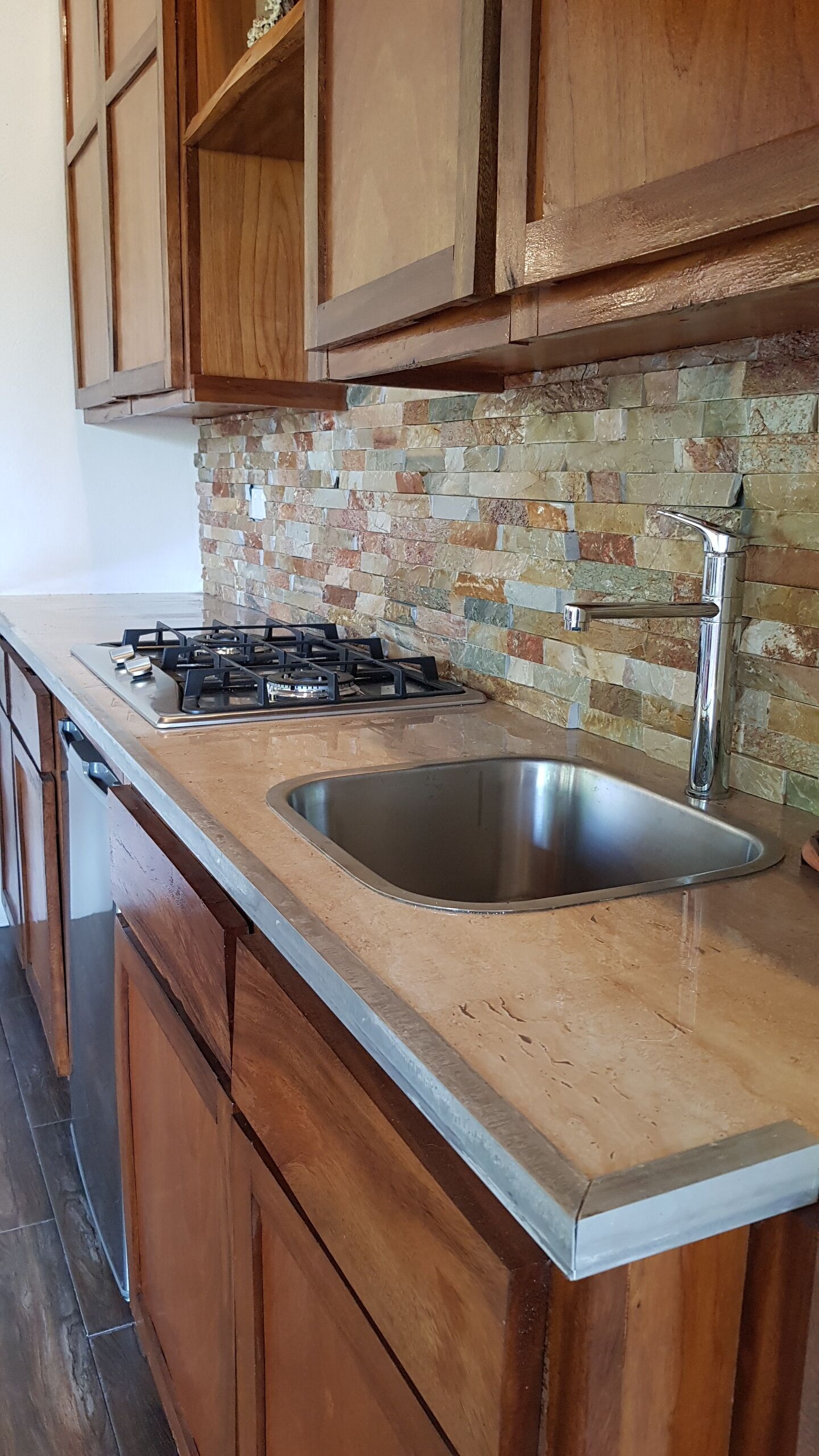 A kitchen with wooden cabinets, a gas stove, a stainless steel sink, and a tiled backsplash.