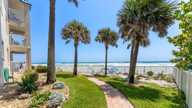 A pathway leading to a beach with palm trees and a building with balconies.