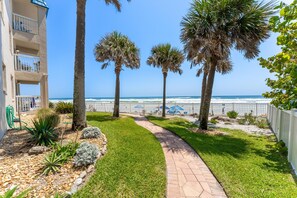 A pathway leading to a beach with palm trees and a building with balconies.
