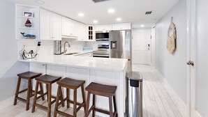 A modern kitchen with white cabinetry, a stainless steel refrigerator, and wooden bar stools.