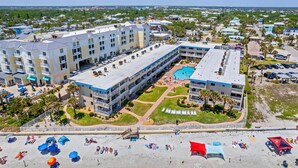 A hotel with multiple floors, a swimming pool, and a beach area with umbrellas.