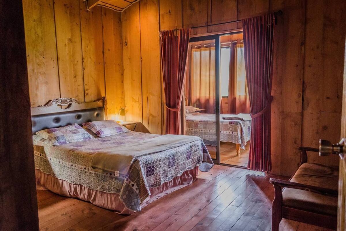 Un dormitorio de cabaña de madera con una cama grande, una silla y una mesa junto a la ventana.