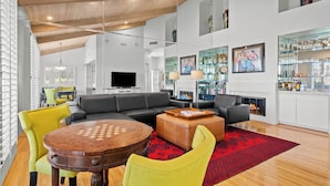 A modern living room with a wooden ceiling, a fireplace, a television, and a dining area with a chess table.