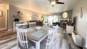 Un salón amplio con una mesa de comedor, sillas blancas, ventilador de techo y chimenea.