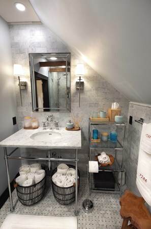 A modern bathroom with a marble sink, a large mirror, and a glass shelf with toiletries.