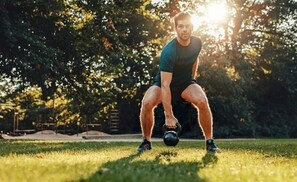 A person performing a squat exercise with a kettlebell in an outdoor setting.