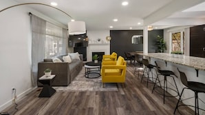 Ein modernes Wohnzimmer mit einem grauen Sofa, gelben Sesseln und einem Essbereich mit Bar.