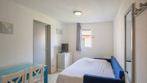 Une chambre à coucher avec un lit, un bureau et une chaise. On y trouve une télévision posée sur une commode et une fenêtre avec des rideaux.