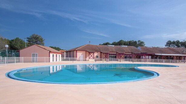 Une piscine entourée d’une terrasse, un petit bâtiment doté d’une porte et un espace couvert avec un toit.