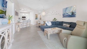 A spacious living area with a large sofa, a coffee table, and a dining area in the background. - Riverwalk Condos - Calm Waters! Overlook the intercoastal! (New Smyrna Beach)