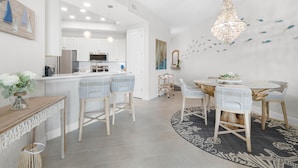 A modern kitchen with white cabinets, a central island with bar stools, and a chandelier. - Riverwalk Condos - Calm Waters! Overlook the intercoastal! (New Smyrna Beach)