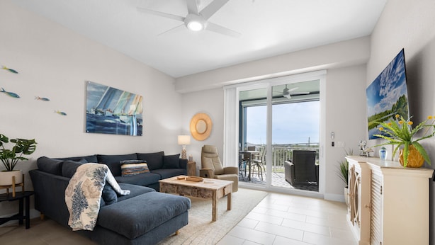 A modern living room with a sofa, coffee table, and a dining area with a table and chairs. There is a balcony with a view of the sea. - Riverwalk Condos - Calm Waters! Overlook the intercoastal! (New Smyrna Beach)