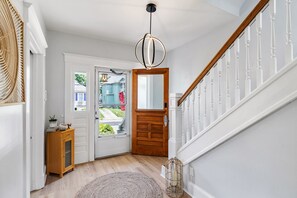Un pasillo con una puerta de madera, un espejo, un mueble pequeño y una cesta de mimbre.