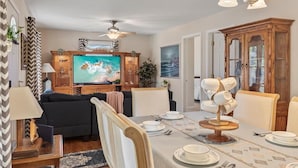 A dining area with a table set for four, a television in the background, and a ceiling fan. - Modern Bungalow Home with Mid-Century Flair (Springfield)