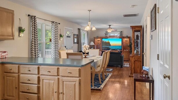 A kitchen with wooden cabinets, a dining area with a table and chairs, and a television in the background. - Modern Bungalow Home with Mid-Century Flair (Springfield)