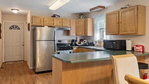 A kitchen with wooden cabinets, a stainless steel refrigerator, a microwave, and a stove. - Modern Bungalow Home with Mid-Century Flair (Springfield)