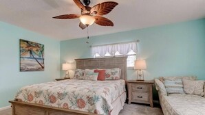A bedroom with a bed, a nightstand, a dresser, a ceiling fan, and a window with curtains.