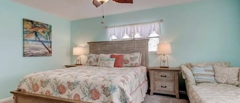 A bedroom with a bed, a nightstand, a dresser, a ceiling fan, and a window with curtains.
