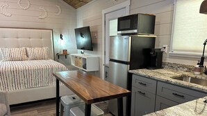 A compact kitchen with a microwave, refrigerator, and a small dining area with stools. - Tiny Home Retreat Near Deep Creek • Hot Tub •Fenced Yard •Perfect Couples Escape (Bryson City)