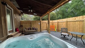 A covered outdoor area with a hot tub, seating, and a wooden fence. - Tiny Home Retreat Near Deep Creek • Hot Tub •Fenced Yard •Perfect Couples Escape (Bryson City)