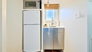 A compact kitchen with a white refrigerator, a microwave, a sink, and a window with a view. - Secluded Windansea Beach Rental Cottage (La Jolla)